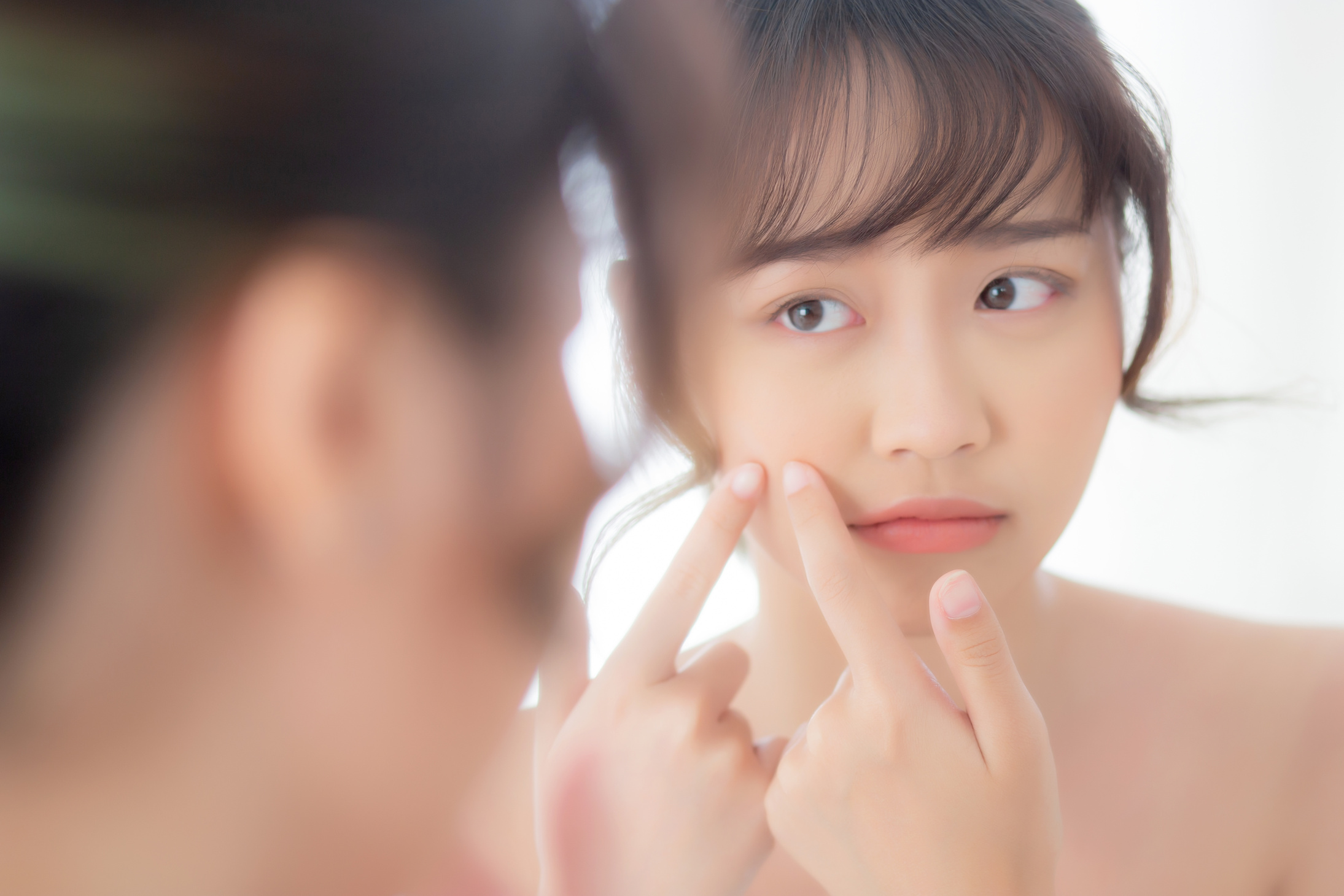 Young Woman's Face in Mirror with Pimple Problem
